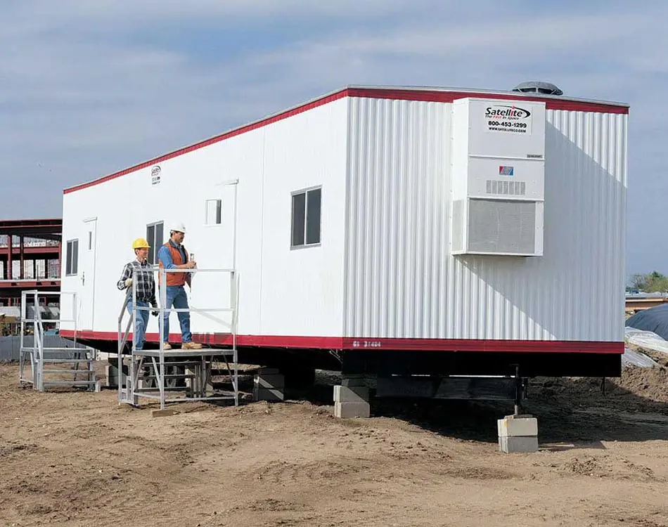 Two men entering a white mobile office trailer.