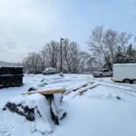 A snowy construction site with materials and equipment covered in snow.