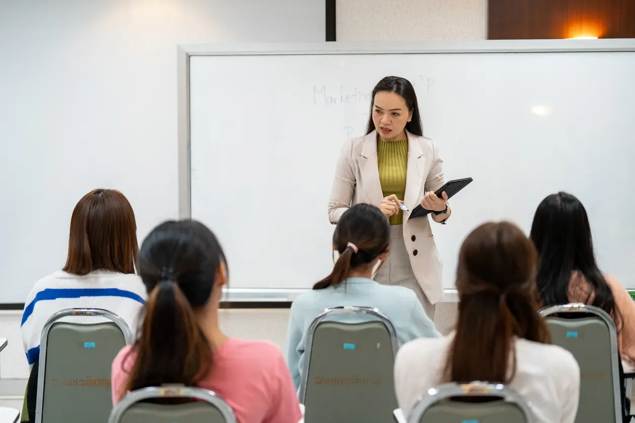 A teacher stands before a whiteboard as she teaches her class.